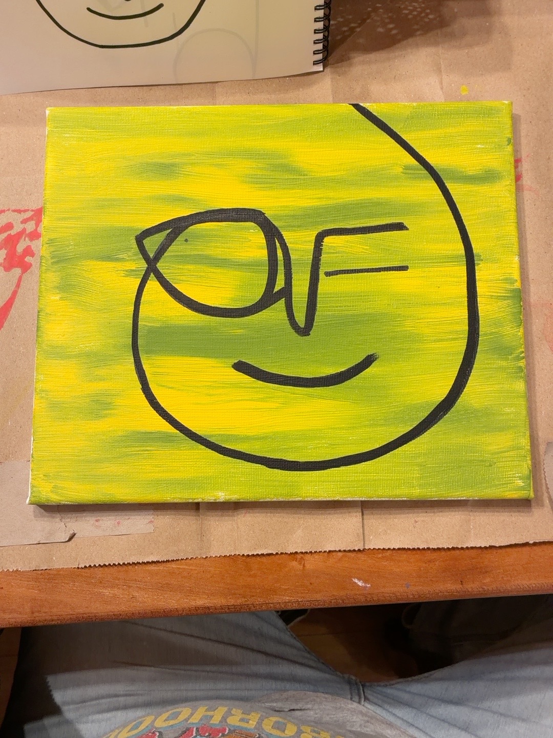Rostro sonriente de líneas negras sobre amarillo y verde.